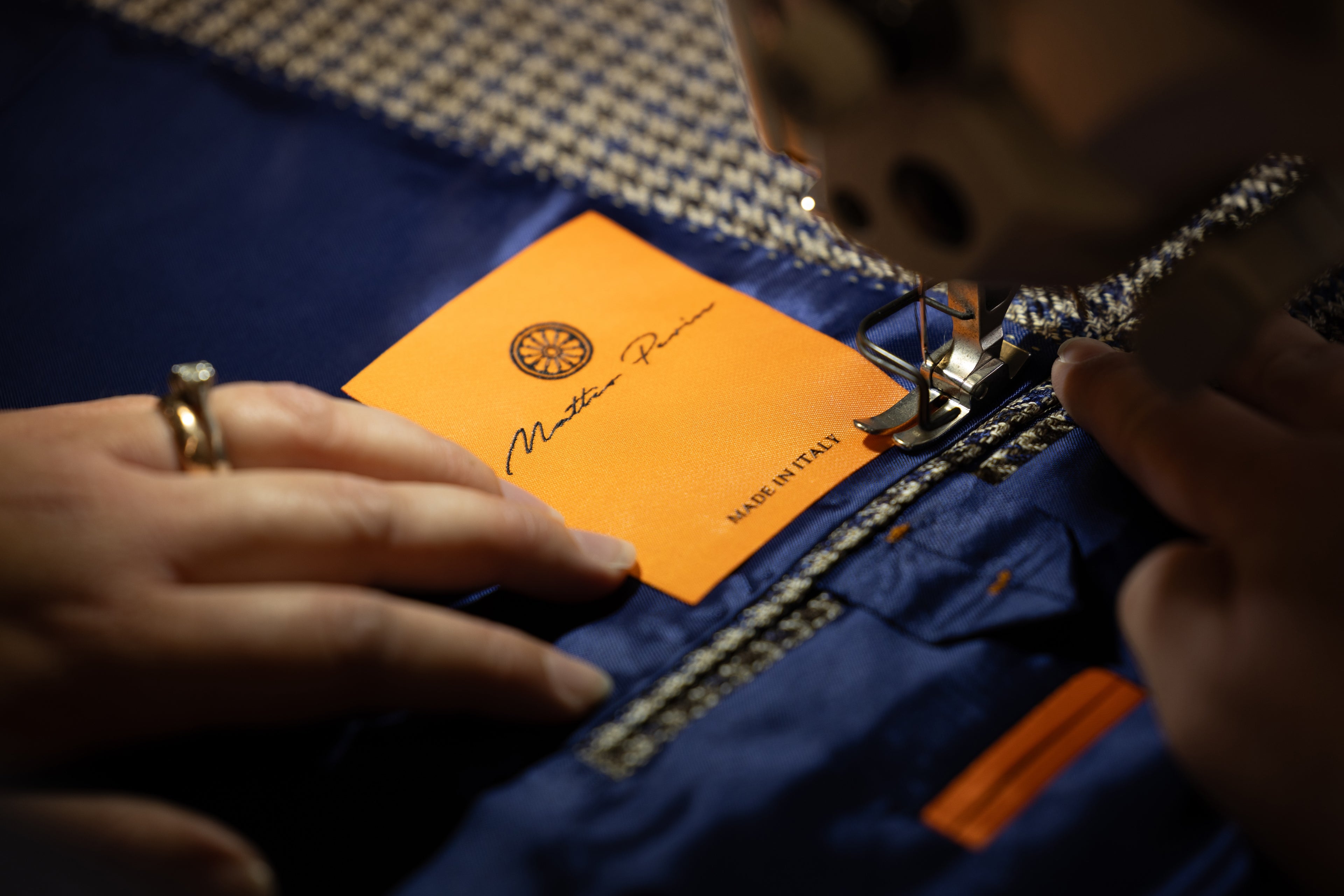 Close-up of a hand guiding fabric with an orange label under a sewing machine, accompanied by a Matteo Perin quote about designing a lifestyle.


